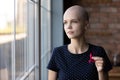 Thoughtful female oncology patient holding red ribbon