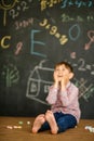 Thoughtful First-grader sits near the school board over the solution of the problem. Hands holding onto his cheeks Royalty Free Stock Photo