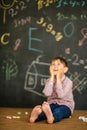 Thoughtful First-grader sits near the school board over the solution of the problem. Hands holding onto his cheeks