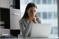 Thoughtful focused young businesswoman looking at laptop screen in office