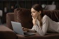 Thoughtful focused woman looking at laptop screen, lying on couch