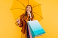 Thoughtful girl, in a bright yellow dress and autumn jacket, standing with a yellow umbrella and shopping bags, on an Royalty Free Stock Photo