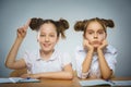 Thoughtful girl and happy girl sitting at desk on gray. school concept Royalty Free Stock Photo