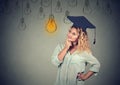 Thoughtful graduate student in cap gown looking up at light bulb Royalty Free Stock Photo