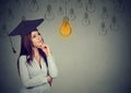 Thoughtful graduate student looking up at bright light bulb Royalty Free Stock Photo