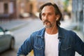 Thoughtful handsome mature grey bearded man with earphones listening music or talking on the phone standing urban street Royalty Free Stock Photo