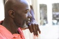Thoughtful, happy senior african american man leaning and looking out of window at home, copy space Royalty Free Stock Photo