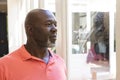 Thoughtful, happy senior african american man standing and looking out of window at home, copy space Royalty Free Stock Photo