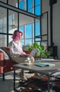 Thoughtful hipster woman pink hair using laptop on sofa thinking of inspiration.