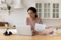 Thoughtful hispanic female hold financial documents look on pc screen