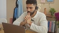 A thoughtful hispanic man with a beard wears a headset while working on a laptop in a cozy home office Royalty Free Stock Photo
