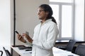 Thoughtful Indian man entrepreneur standing in office with smartphone