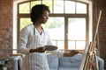 Thoughtful inspired African artist woman in apron working in studio