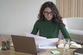 Thoughtful Italian female freelancer in glasses sitting at desk, holding papers and preparing report