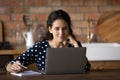 Thoughtful latin woman watch webinar on laptop at home kitchen Royalty Free Stock Photo