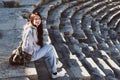 Thoughtful lonely pretty young woman sits on the steps in ancient amphitheater