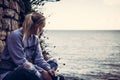 Thoughtful lonely young woman tourist with closed eyes thinking during her travel sitting on seashore in retro vintage style