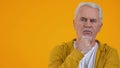 Thoughtful male pensioner on orange background, choice hesitation, problem