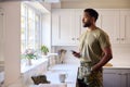 Thoughtful Male Soldier In Uniform With Mobile Phone In Kitchen On Home Leave Looking Out Of Window Royalty Free Stock Photo