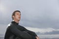 Thoughtful Male Surfer Sitting Against Cloudy Sky At Beach