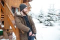 Thoughtful man with beard standing near log cabine in winter