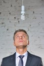 Thoughtful mature businessman looking at energy efficient lightbulb hanging against brick wall at office Royalty Free Stock Photo