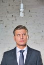 Thoughtful mature businessman looking at energy efficient lightbulb hanging against brick wall at office Royalty Free Stock Photo