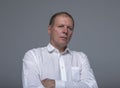 Thoughtful mature caucasian businessman over gray background with crossed arms looking down. Calm tired pensive man