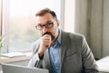 Thoughtful middle aged handsome businessman in shirt working on laptop computer in office