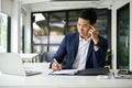 Thoughtful millennial Asian businessman rechecking business documents at his desk Royalty Free Stock Photo