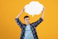 Thoughtful millennial guy holding empty speech bubble over orange studio background, space for your ad design Royalty Free Stock Photo