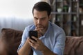 Thoughtful millennial man rubbing chin reading important phone message Royalty Free Stock Photo