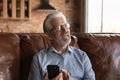 Thoughtful old man sit on couch hold phone look aside Royalty Free Stock Photo