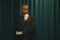 thoughtful portrait of an african american man wearing white gloves. background green curtain drape