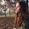 Portrait of a young girl with long hair, sitting at the park, staring far away daydreaming Royalty Free Stock Photo