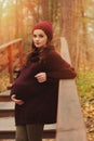 Thoughtful pregnant woman in soft warm cozy marsala outfit walking outdoors