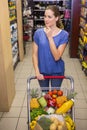 Thoughtful pretty woman pushing trolley in aisle Royalty Free Stock Photo