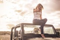 Thoughtful pretty young blonde caucasian girl sitting on his convertible car with nude feet - relax for a traveler with sunset