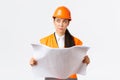 Thoughtful professional asian female construction manager, architect reading blueprints and looking away pondering Royalty Free Stock Photo