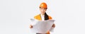 Thoughtful professional asian female construction manager, architect reading blueprints and looking away pondering Royalty Free Stock Photo