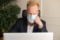 Thoughtful red-haired businessman in smart casual suit wearing protective face mask