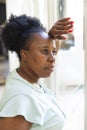 Thoughtful, sad senior african american woman standing looking out of window at home Royalty Free Stock Photo