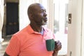 Thoughtful senior african american man having coffee and looking out of window at home Royalty Free Stock Photo