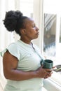 Thoughtful senior african american woman having coffee looking out of window at home Royalty Free Stock Photo