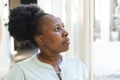 Thoughtful senior african american woman standing looking out of window at home Royalty Free Stock Photo