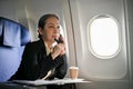 A thoughtful senior Asian businesswoman is on the phone with her client during the flight