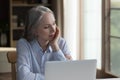 Thoughtful serious elder woman sitting at laptop computer at home