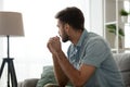 Thoughtful serious man sitting on sofa at home, lost in thoughts