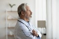 Thoughtful serious senior doctor looking through window lost in thoughts