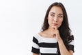 Thoughtful and sly young asian brunette girl in striped t-shirt, touching chin and looking sideways with suspicious Royalty Free Stock Photo